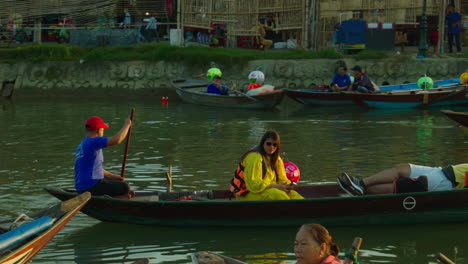 Woman-tourist-clicking-selfies-while-having-ride-on-wooden-traditional-boat-in-the-ancient-town-of-Hoi-An-with-other-boats-and-tourists-at-backdrop,-Vietnam