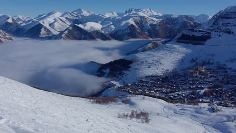 Aerial-time-lapse-of-low-clouds-in-the-high-snowy-mountain-advancing-towards-a-village-on-a-sunny-day