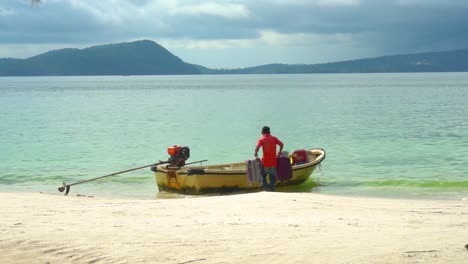Man-loads-travel-cases-into-a-small-water-taxi-boat-on-the-shore-of-a-tropical-beach