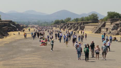 Handheld-shot-of-a-crowd-of-tourists-walking-through-the-archaeological-site-of-Teotihuacan-in-Mexico,-with-the-ancient-Pyramid-of-the-Sun-in-the-background,-on-a-clear-and-sunny-day