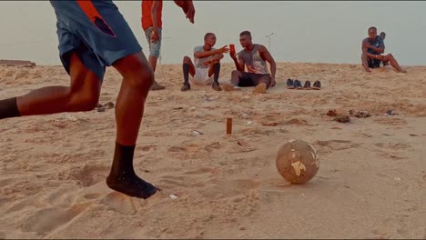 Low-shot-kicking-soccer-ball-on-beach-at-golden-hour,-tracking-shot