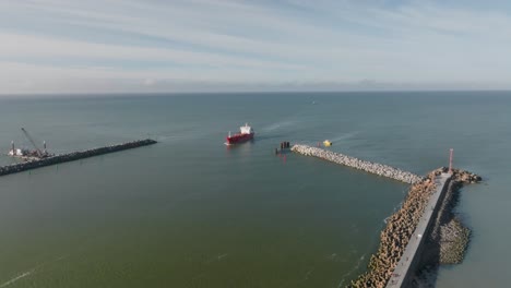 Aerial-view:-a-red-cargo-ship-sails-through-the-port-gates-of-Klaipeda-city