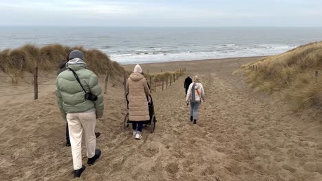 Family-Group-walking-downhill-the-sandy-dunes-towards-North-Sea-in-Netherlands---Slow-motion-footage