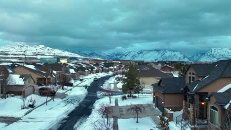 Snowy-neighborhood-at-sunrise-or-sunset-below-the-mountains---aerial-flyover