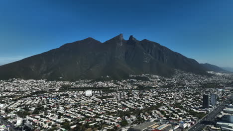 Vista-Aérea-Sobre-El-Paisaje-Urbano-De-Monterrey-Con-El-Cerro-De-La-Silla-En-El-Fondo,-En-El-Soleado-México