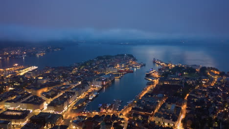 Aerial-shot-going-down-through-the-clouds-to-reveal-the-city-of-Bergen,-Norway-at-night