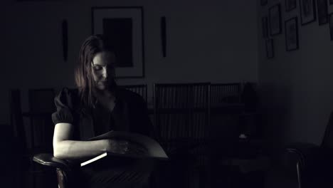 Woman-sitting-in-a-darkened-room-paging-through-a-coffee-table-photography-book