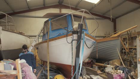 Young-apprentice-shipwright-boards-fiberglass-boat-to-inspect-gunwale