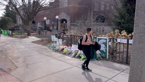 Union-building-on-the-campus-of-Michigan-State-University,-site-of-a-mass-shooting-on-February-13,-2023-with-flower-memorial-and-young-woman-walking-by