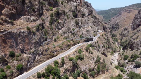 Aerial-view-of-cars-driving-through-a-dangerous-narrow-road-between-rocky-canyon-at-day-time