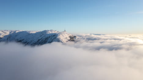 Drone-shot-just-above-inversion-clouds-showing-a-winter-landscape-with-mountains-in-Bergen,-Norway