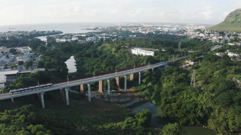 Aerial-view-of-metro-crossing-river-on-bridge-in-rural-area-of-Mauritius-at-sunset-time