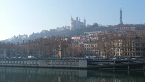 Blick-Hinauf-Zur-Dunstigen-Hügelbasilika-Notre-Dame-De-Fourvière-Vom-Stadtfluss-Lyon,-Frankreich-Bei-Sonnenaufgang