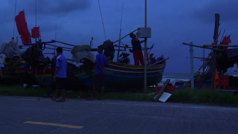 People-caring-for-traditional-wooden-boats-in-dangerous-windy-weather-at-night,-Songkhla-in-Thailand