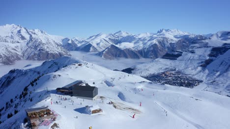 4K-Luftaufnahme-Eines-Skigebiets-Mit-Menschen,-Die-An-Einem-Sonnigen-Tag-Hoch-Oben-In-Den-Schneebedeckten-Bergen-Der-Alpen-Ski-Fahren