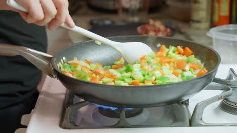 Vegetables-being-stirred-in-a-frypan-by-caucasian-male-hand-on-gas-stove