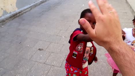 Tourist-man-playing-with-some-African-kids-by-high-fiving-them-in-a-street-of-Zanzibar,-Tanzania