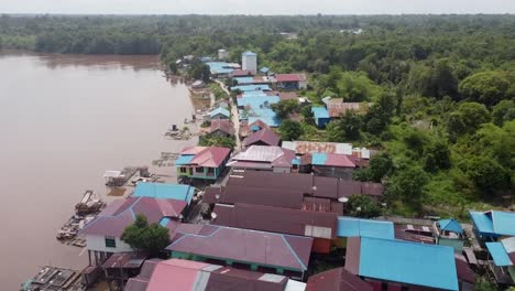 Drone-zoom-out-of-a-small-tropical-village,-as-it-zooms-out-it-reveals-the-surrounding-jungle-and-the-houses-near-the-river