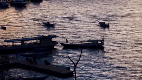Silhouetted-people-during-dusky-evening-light-working-on-unloading-small-boats-in-Labuan-Bajo-harbour-on-Flores-Island,-Indonesia