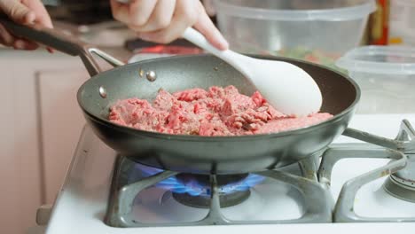 Caucasian-male-hand-breaking-up-raw-mince-meat-in-pan-over-gas-burner