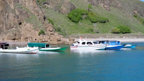 Moored-boats-in-a-secluded-white-sandy-beach-beach-with-turquoise-water-and-rugged-mountains-on-tropical-Padar-Island-in-Komodo-National-Park,-East-Nusa-Tenggara,-Indonesia