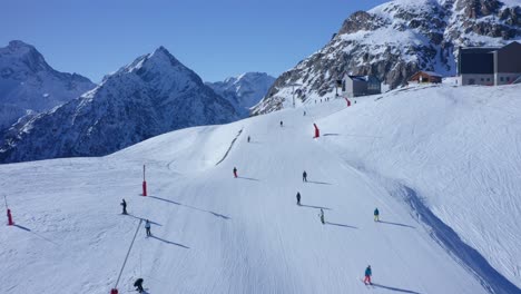 Luftaufnahme-Von-Mehreren-Skifahrern,-Die-An-Einem-Sonnigen-Tag-Einen-Verschneiten-Hang-Auf-Einem-Berggipfel-Fahren