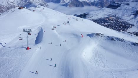 Aerial-gimbal-down-revealing-several-skiers-skiing-down-a-snowy-mountain-slope-in-the-Alps