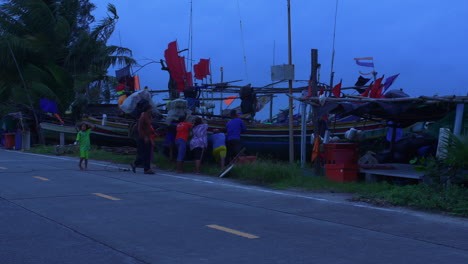 Gruppe-Von-Menschen,-Die-Bei-Starkem-Wind-Ein-Traditionelles-Thailändisches-Holzboot-Am-Ufer-Schieben,-Songkhla,-Thailand