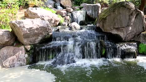 Slowmotion-tilting-upward-shot-of-a-small-waterfall-cascade-in-a-Japanese-Garden