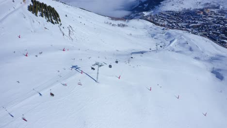 Vista-Aérea-De-Una-Pista-De-Esquí-De-Alta-Montaña-Con-Gente-Esquiando-Y-Remontes-Corriendo-En-Un-Día-Soleado