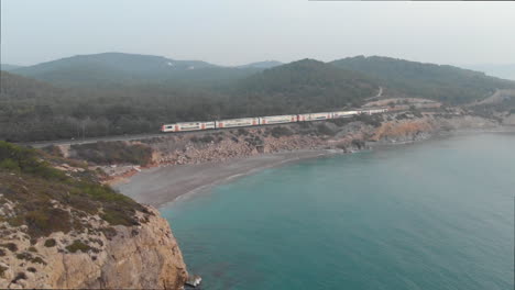 Flying-drone-above-rocky-coast-while-train-passes-by