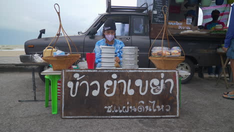 Hombre-Asiático-Vendiendo-Comida-Rápida-Casera-En-Un-Puesto-De-Comida-En-La-Playa-En-Tailandia