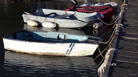 Kleine-Alte-Boote,-Die-Mit-Seilen-Am-Dock-Befestigt-Sind-Und-Sich-Langsam-Auf-Dem-Wasser-Bewegen