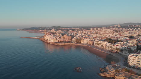 Drone-aerial-view-lowering-over-bay-,-Spanish-coastal-town-during-golden-hour
