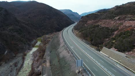 Scenic-view-of-mountain-road-leading-through-river-valley-with-cars-driving,-highway-in-Albania