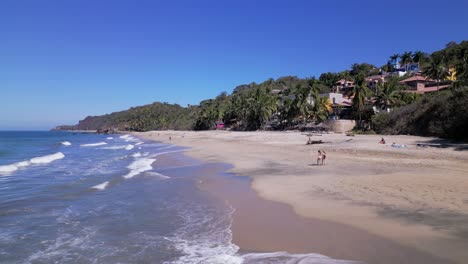 2-women-walk-along-the-beach-of-Sayulita-Mexico-with-waves-crashing-near-them-as-seen-from-an-aerial-drone-point-of-view