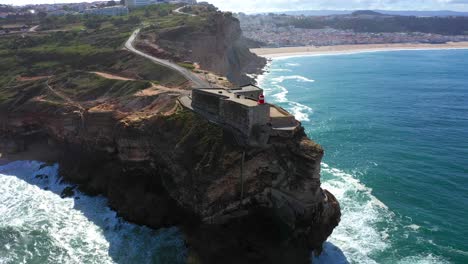 Aerial-view-of-lighthouse-in-Nazaré-with-steep-high-rocky-cliff