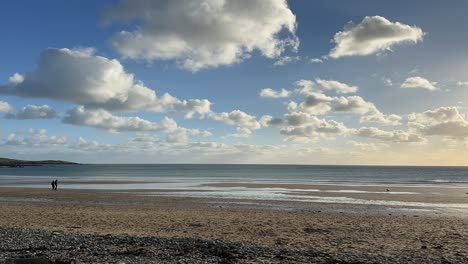 Puff-white-clouds-passing-on-a-blue-sunny-winter-sky-while-people-walking-on-a-sandy-beach-in-time-lapse-video