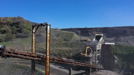 Panning-shot-of-dump-truck-loading-conveyor-belt-in-a-quarry