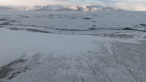 Dolly-Vorwärts-über-Schneebedecktem-Ufer,-Zugefrorenem-See-Und-Bergen,-An-Sonnigen-Tagen,-Island