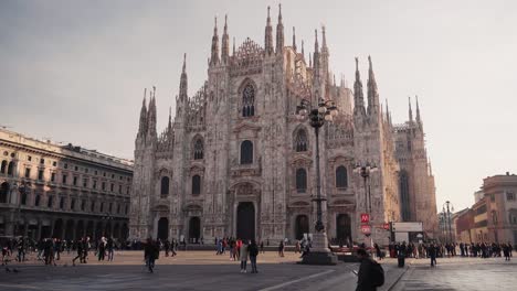 Frontal-view-of-Duomo-Milano-Cathedral-in-Milan-with-people-walking-on-open-square,-camera-movement,-downtown-view-of-Italian-city-with-tourists