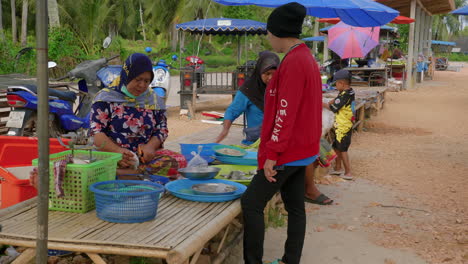 Old-woman-selling-fish-to-customer-in-street-food-stall-in-Songkhla,-Thailand
