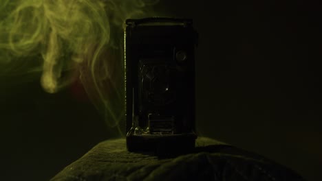 Yellow-smoke-behind-a-very-old-vintage-folding-camera-from-1910-in-a-dark-room