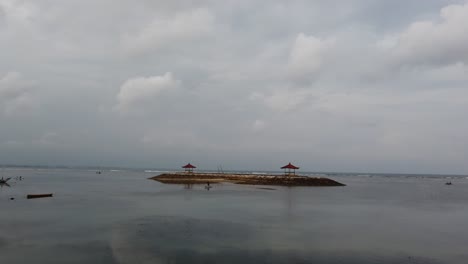 Pavillon-Pagode-Schwimmt-Am-Strand-Von-Sanur,-Bali,-Indonesien.-Bewölktes-Wetter,-Blaues-Meer,-Weiße-Skyline.-Ein-Mann-Paddelt-Mit-Seinem-Kanu,-Indonesien,-Ruhige-Wellen