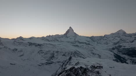Stunning-mountain-drone-aerial-with-epic-view-of-Matterhorn-Zermatt-in-Swiss-Alps-at-Sunset-during-winter-with-golden-clear-sky-and-airplane-flying-over