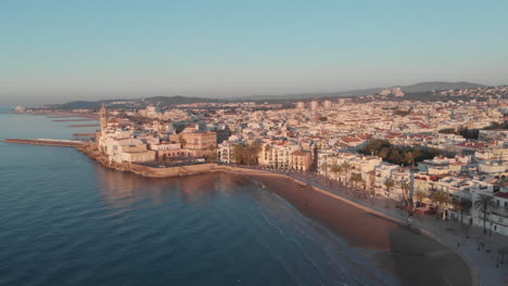 Flying-drone-above-coastal-sunny-European-city,-buildings-pier-and-mountains