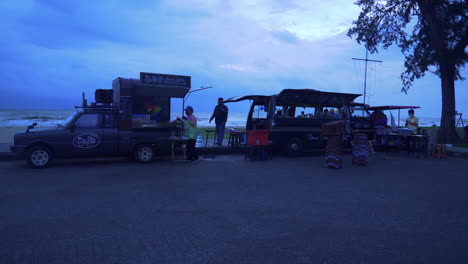 Camiones-De-Comida-Y-Gente-En-El-área-De-Recreación-Local-Y-La-Playa-A-La-Luz-De-La-Tarde,-Tailandia