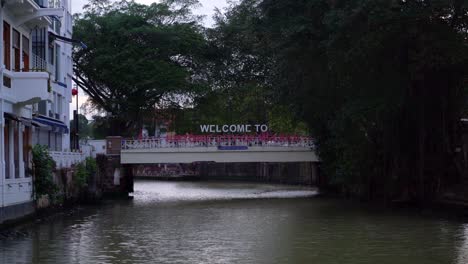 Vista-Pacífica-Del-Río-Del-Puente-Y-El-Cartel-De-Bienvenida-A-La-Histórica-Ciudad-De-Malaca,-Malasia