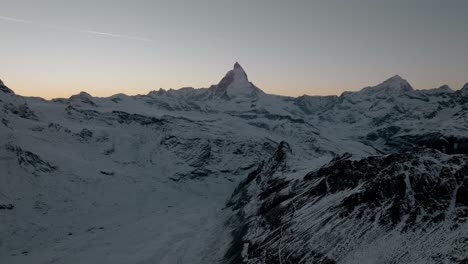 Mountain-drone-aerial-with-stunning-view-of-Matterhorn-Zermatt-in-Swiss-Alps-at-Sunset-during-winter-with-golden-clear-sky-and-airplane-flying-over
