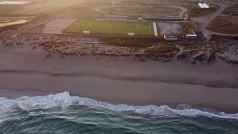 Aerial-tilt-up-shot-of-Atlantic-Ocean,-Beach-and-Soccer-Stadium-of-Vila-do-Conde-in-Portugal---Descending-shot-on-green-lawn